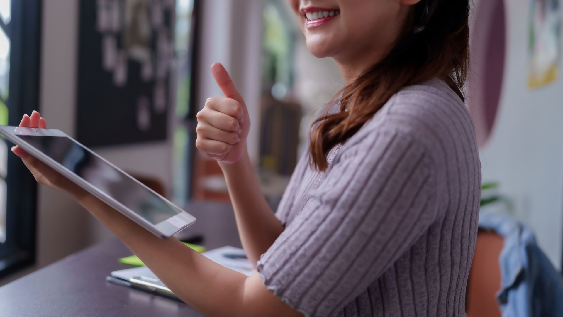 Asian adult woman showing success achievement using digital tablet technology at modern coworking space office environment for remote work